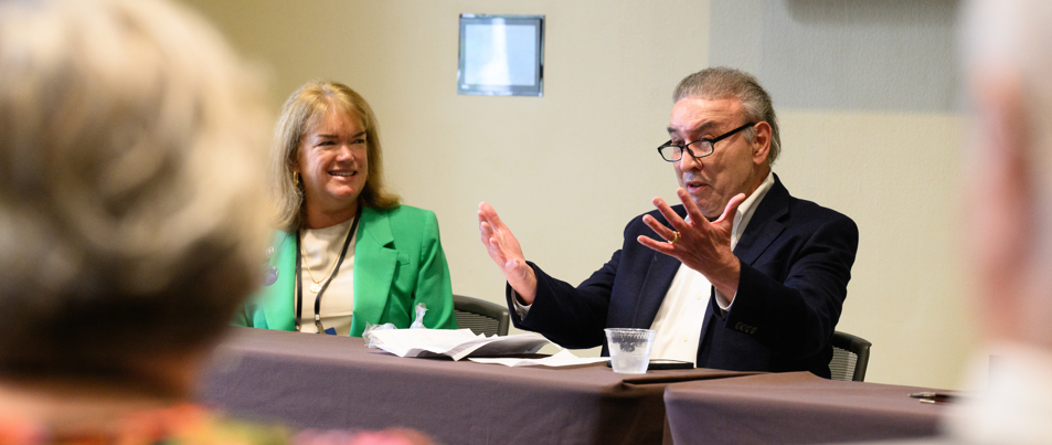 A picture of Lisa Butler wearing a green blazer smiling at Ralph G. Neas who is wearing a dark blue suit jacket with his hands raised speaking to a crowd of people.